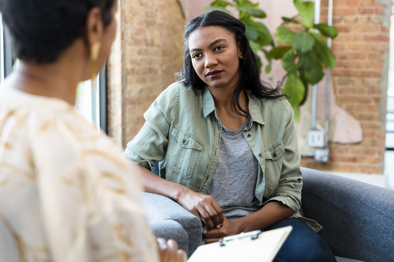 A patient talking to a counselor who is holding a notebook.